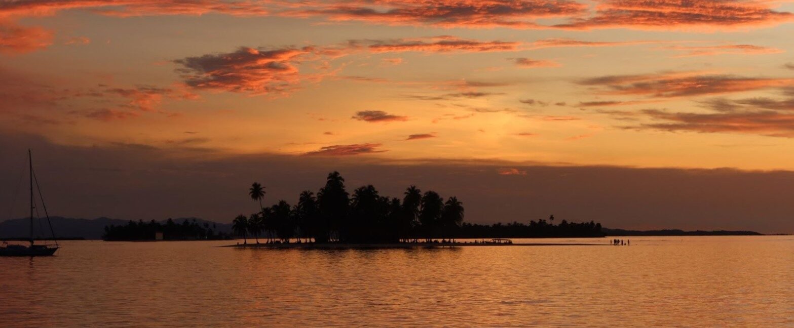 Caribbean Sunset in the San Blas Islands Orange sunset over a palm-covered island in San Blas, with a sailboat anchored nearby.